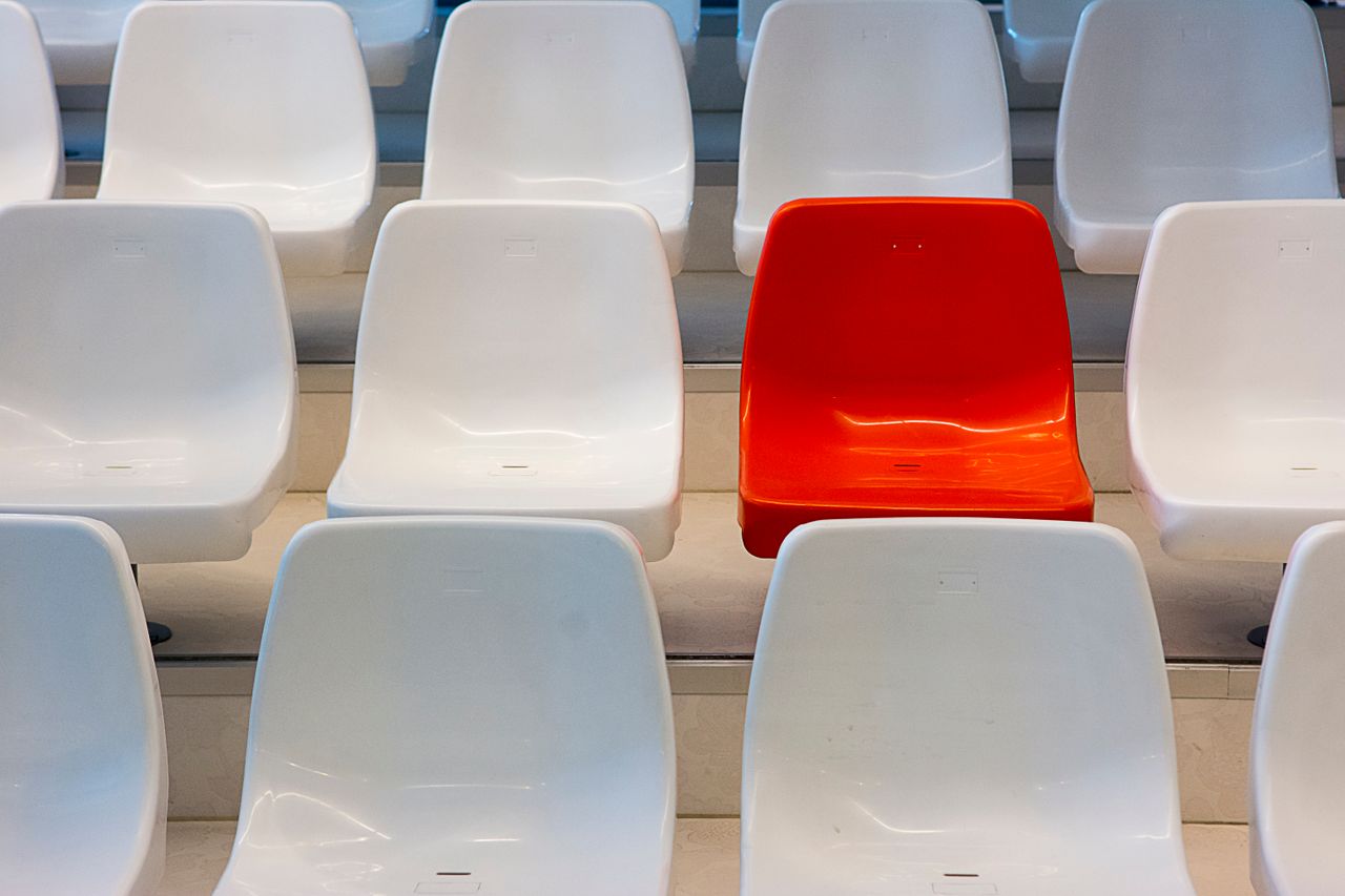 A vibrant red chair stands out among rows of white seats in an auditorium setting.